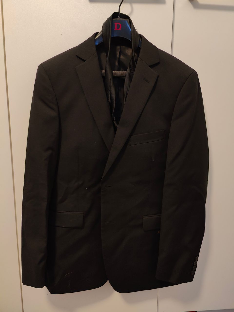 Musta puku, kauluspaita, kravaatti ja pukupussi