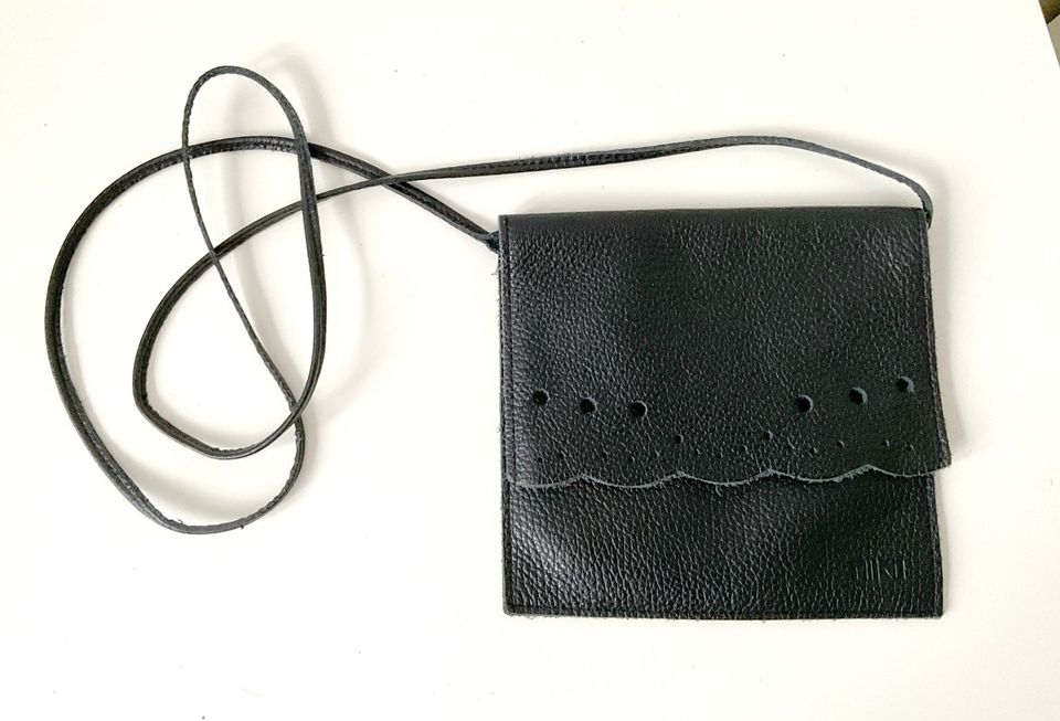 Pieni musta aitoa nahkaa oleva laukku / clutch olkahihnalla. Leikkaa koristeita