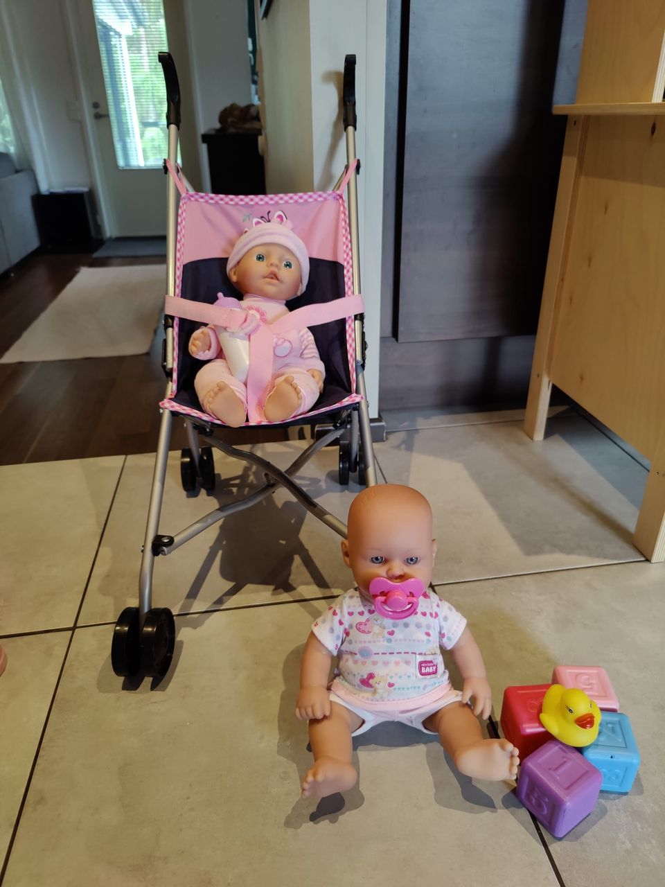 Kaksi vauvanukkea, nukenrattaat ja tarvikkeita