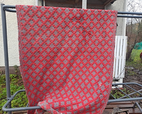 Punainen ja harmaa käsinkudottu matto.