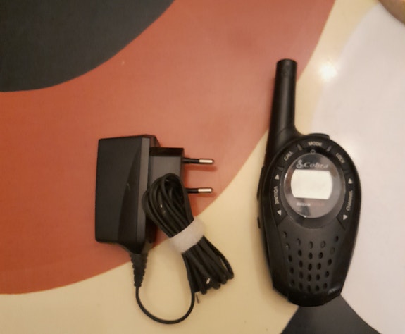 Puhelimen käyttömätön laturi ja käytetty kopra radiopuhelin