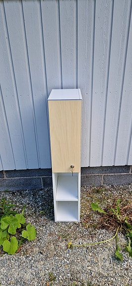 Kapea valkoinen säilytyskaappi ovella ja hyllyillä.